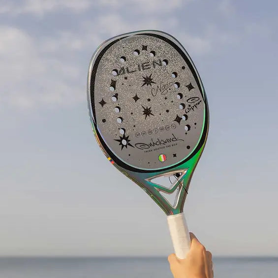 Quicksand Alien 2025 beach tennis racket held by a hand with a beach and sky background