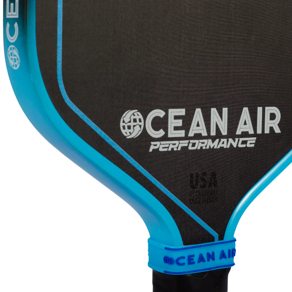 Close-up of a pickleball paddle with 'Ocean Air Performance' branding on a black and blue background.